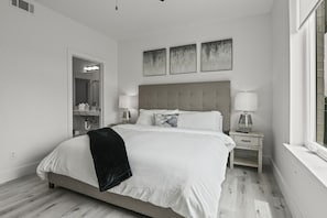 Une chambre à coucher moderne avec un grand lit, des tables de chevet, un miroir et des œuvres d’art accrochées au mur.