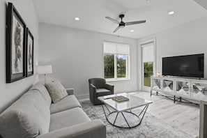 A modern living room with a sofa, armchair, coffee table, and a TV on a cabinet. - Brand New 2 Bedroom Condo-Luxurious Waterfront Pool-Sleeps 4 (Gulfport)