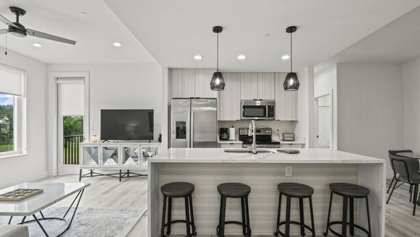 A modern kitchen with a central island, bar stools, a flat-screen TV, and stainless steel appliances. - Brand New 2 Bedroom Condo-Luxurious Waterfront Pool-Sleeps 4 (Gulfport)