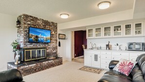 A living room with a brick fireplace, a flat-screen TV, a leather sofa, and a kitchen area with white cabinets and a microwave. - Red Hills Vacation | 3BR Hot Tub, Sauna & Views (Dundee)