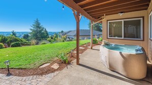 A covered patio with a hot tub, a clear view of the landscape, and a well-maintained lawn. - Red Hills Vacation | 3BR Hot Tub, Sauna & Views (Dundee)