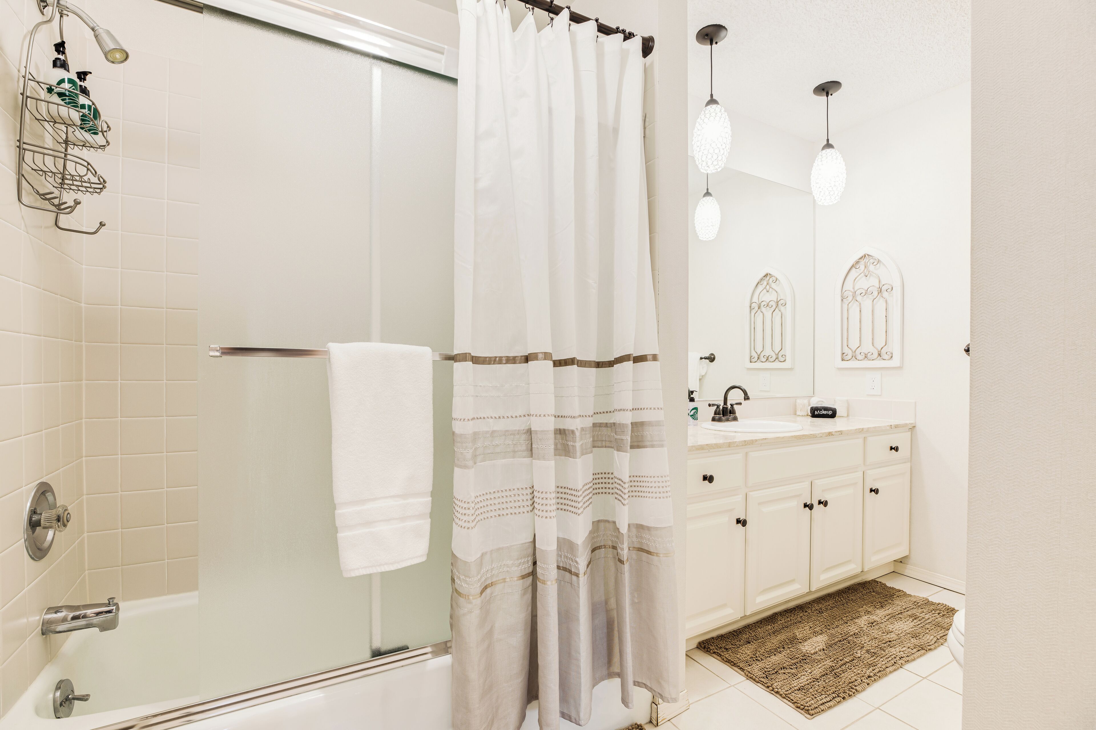 A bathroom with a glass shower enclosure, a white bathtub, a white sink with a mirror, and a patterned rug.