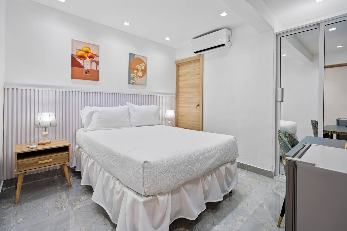 Een moderne slaapkamer met een groot bed, bedlampen, een houten deur en een klein tafeltje met een stoel.