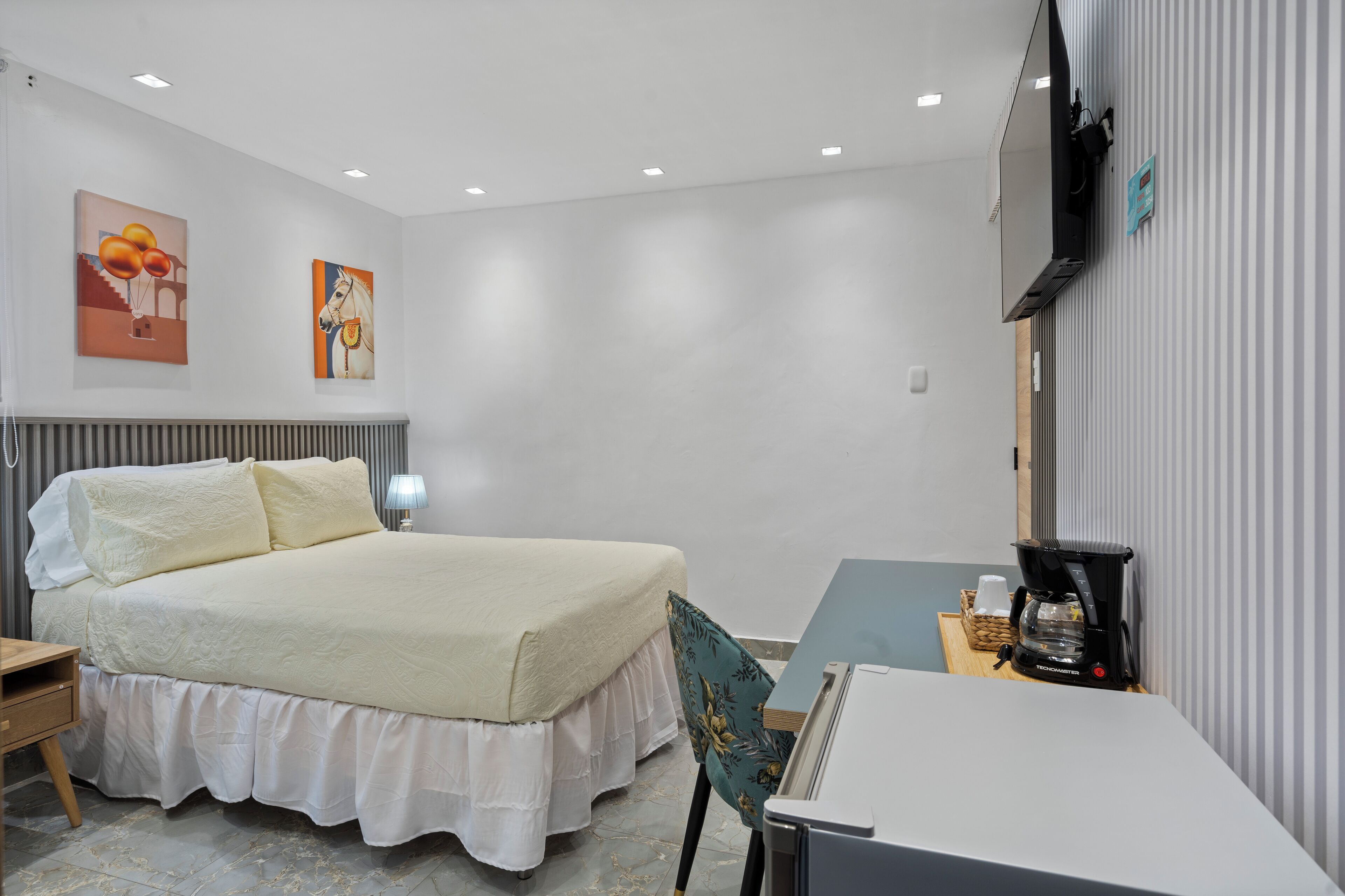 A neatly arranged hotel room with a bed, bedside table, lamp, and a coffee maker on a small table.