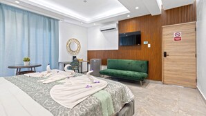 A modern hotel room with a large bed, a green sofa, a small table with a plant, and a TV mounted on the wall.