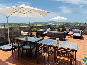 Un patio al aire libre con mobiliario de madera, paredes de piedra y sombrillas blancas.
