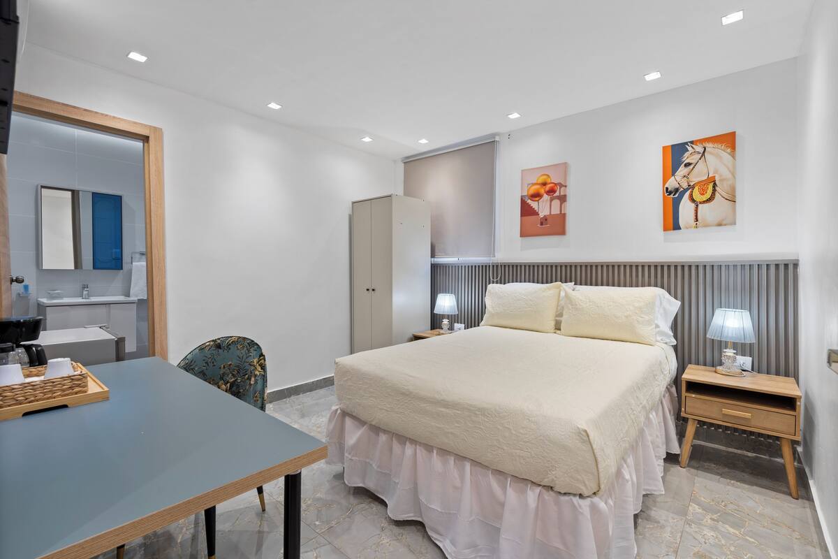 Een hotelkamer met een bed, nachtkastjes, een bureau, een stoel, een kledingkast en kunstwerken aan de muur.