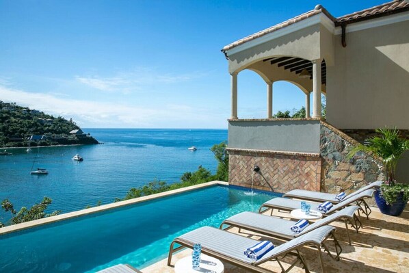 Un área de piscina con sillones de descanso y vista al mar.