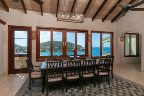 Comedor con vistas al mar y las colinas, muebles de madera y un ventilador de techo.