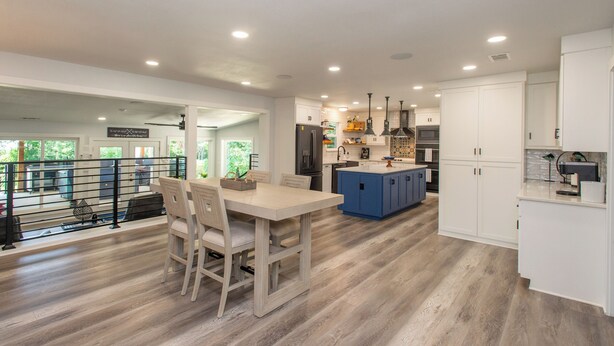 A modern kitchen with white cabinetry, a blue island, and a dining area with a wooden table and chairs. - Gorgeous Modern Lakeside Getaway in Gun Barrel City (Gun Barrel City)