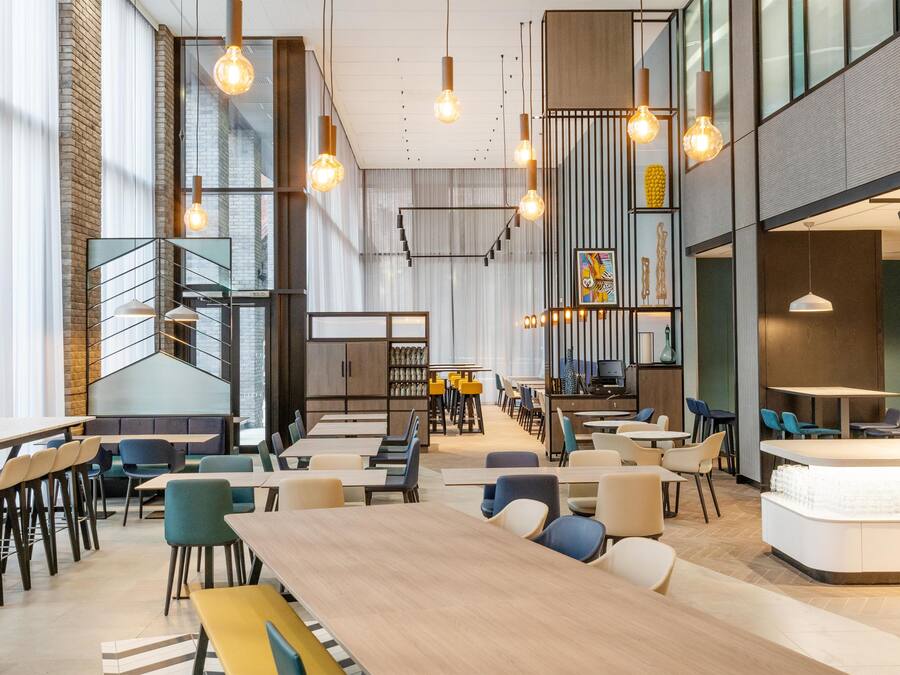 A modern interior with high ceilings, exposed brick walls, and a mix of seating arrangements including tables and booths.