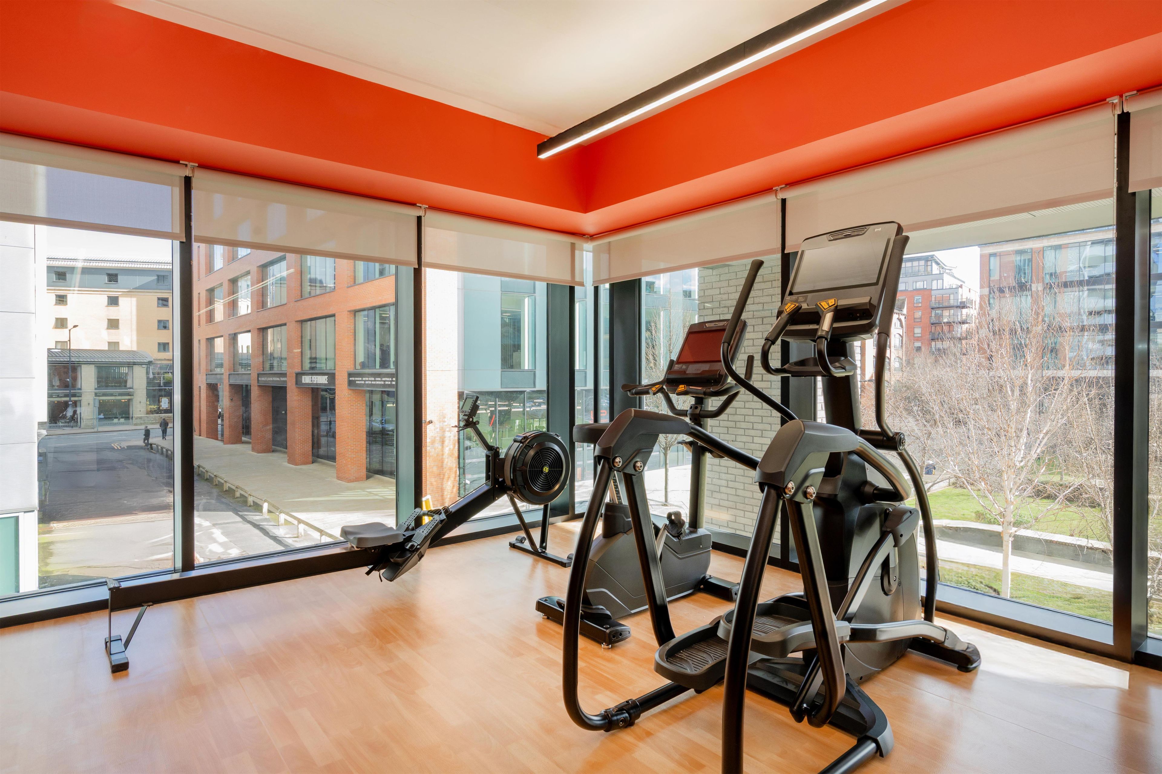 A gym with cardio equipment and large windows overlooking a cityscape.