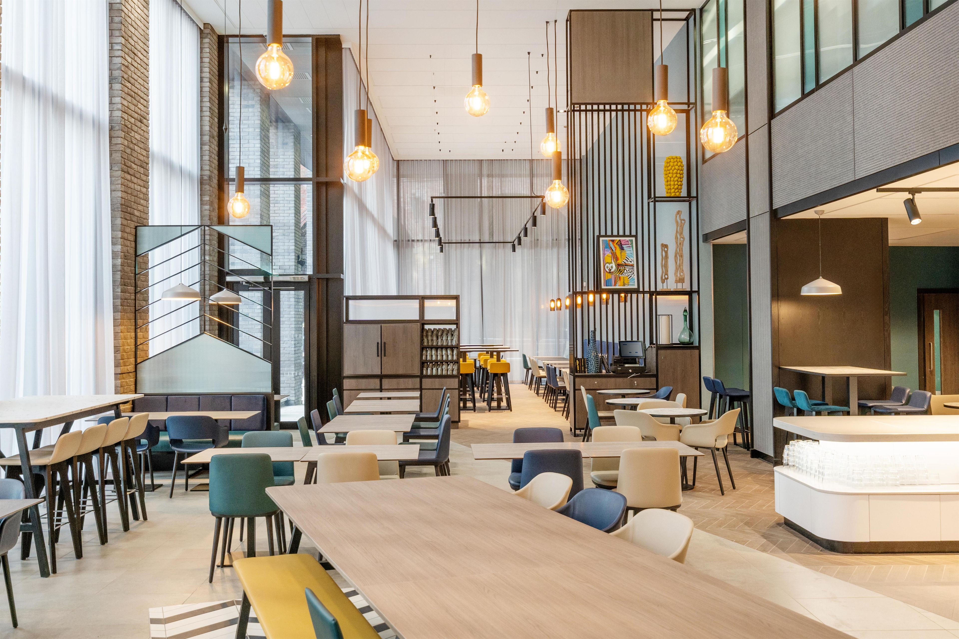 A modern interior with high ceilings, exposed brick walls, and a mix of seating arrangements including tables and booths.