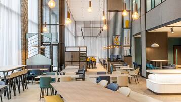 A modern interior with high ceilings, exposed brick walls, and a mix of seating arrangements including tables and booths.