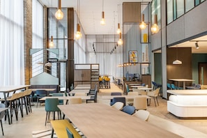 A modern interior with high ceilings, exposed brick walls, and a mix of seating arrangements including tables and booths.