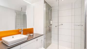 A modern bathroom with a glass shower enclosure, a white sink, and an orange accent wall.