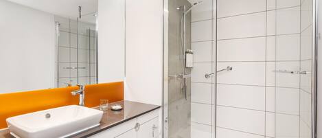 A modern bathroom with a glass shower enclosure, a white sink, and an orange accent wall.