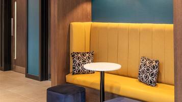 A modern interior with a yellow sofa, two patterned cushions, a round white table, and a blue ottoman.