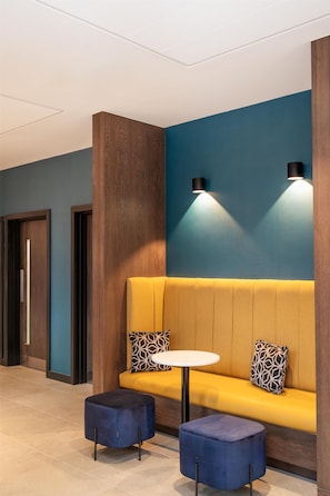 A modern interior with a yellow sofa, two patterned cushions, a round white table, and a blue ottoman.