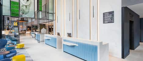 A modern hotel lobby with a reception desk, seating area, and a large glass wall with artwork.