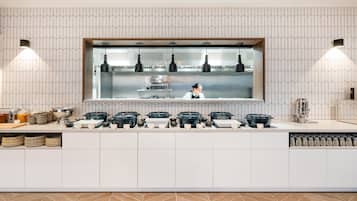 Una cocina moderna con una isla central, iluminación colgante y un chef preparando comida.