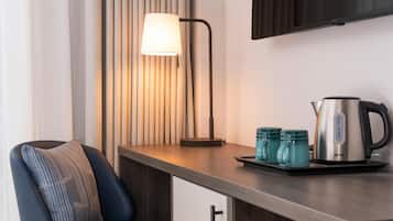A modern kitchenette with a chair, a lamp, a kettle, and a flat-screen TV mounted on the wall.
