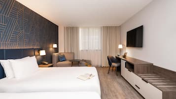 A hotel room with a bed, a desk, a chair, a TV, and a window with curtains.