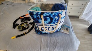 A bed with a grey bedspread, a blue and white bag labeled "ESCAPADE" containing items like a snorkel, goggles, and a brochure. - Your tropical studio steps from the beach. (St Thomas)