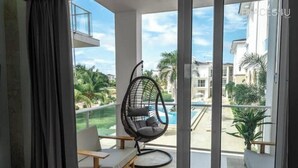 Un balcón con una silla colgante, un sofá y vistas a una piscina y edificios.