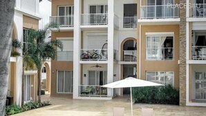 Un edificio de varios pisos con balcones, un patio cubierto con sillas y una sombrilla, y bicicletas estacionadas en el piso superior.
