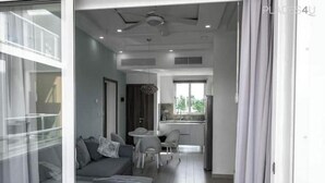 Una sala de estar moderna con un sofá, una mesa de comedor y sillas. Se observa un área de cocina al fondo, con una ventana.