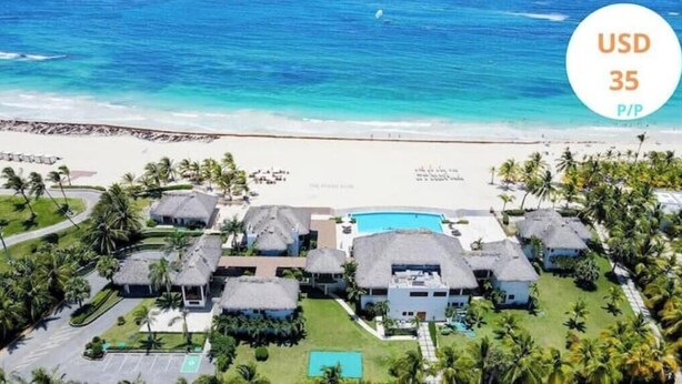 Un resort frente a la playa con bungalows de techo de paja, una piscina y vista al mar.