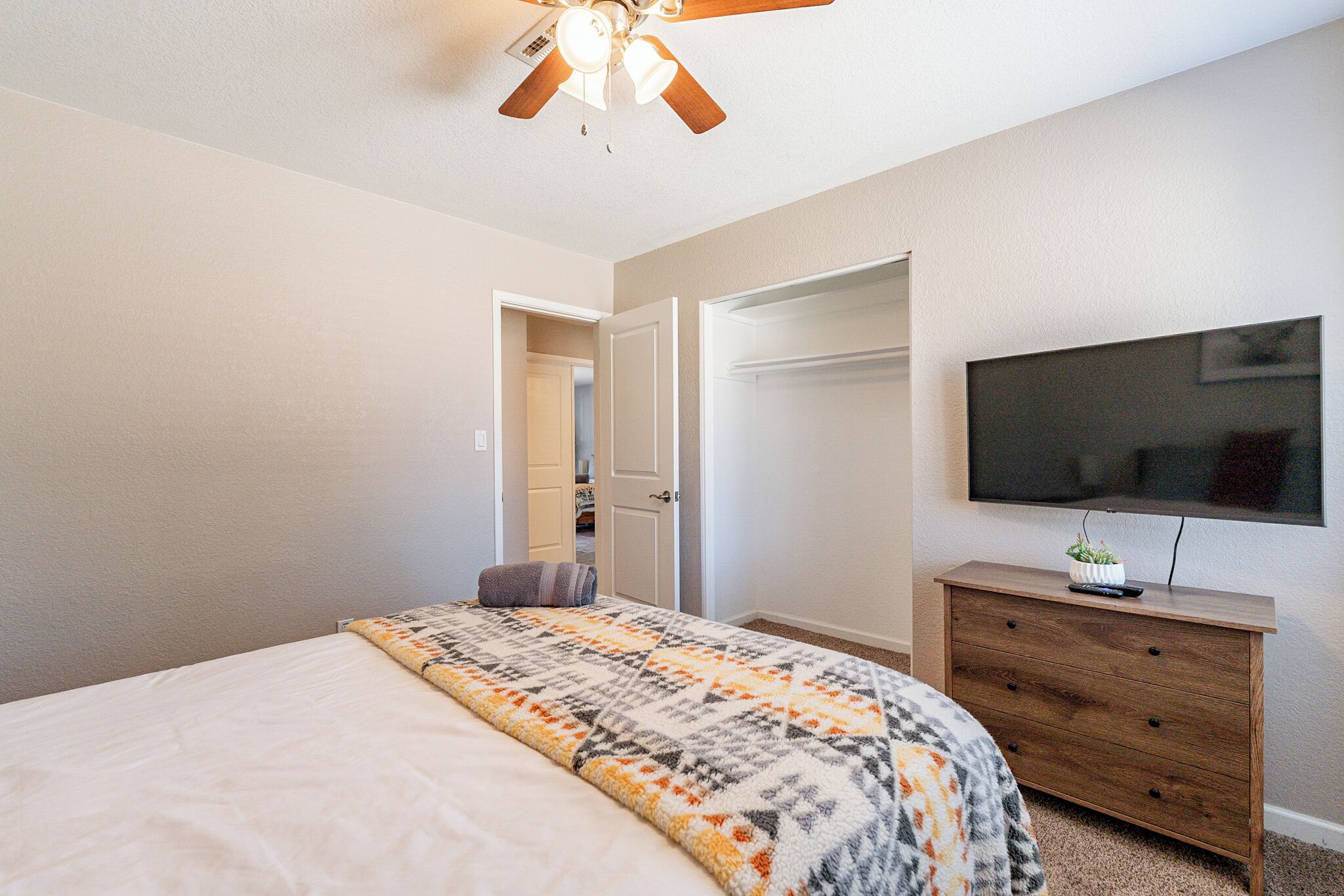 A bedroom with a bed, a dresser, a TV, and a ceiling fan.