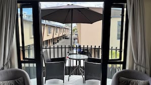 Un balcón con mesa y sillas, vista a la calle y un paraguas grande.