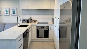 Una cocina moderna con armarios blancos, horno empotrado, lavavajillas y refrigerador de acero inoxidable.
