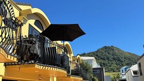 Un edificio amarillo con balcones, un espacio al aire libre cubierto y una montaña al fondo.