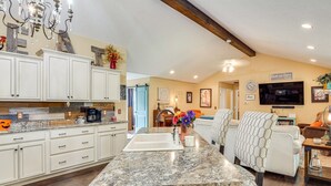 A spacious kitchen with white cabinets, a granite countertop, and a dining area with a hexagonal patterned chair.