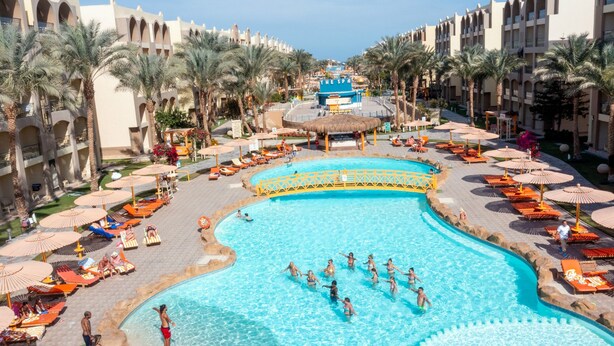 A large pool surrounded by palm trees and sun loungers, with a building in the background. - Go Egypt Luxe Living Apartments (Hurghada)