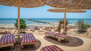 A beachside resort with sunbeds, umbrellas, and a pier in the background. - Go Egypt Luxe Living Apartments (Hurghada)