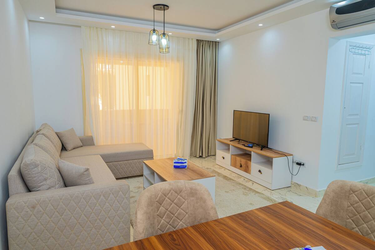 A modern living room with a sofa, a wooden coffee table, a TV stand, and a dining area.