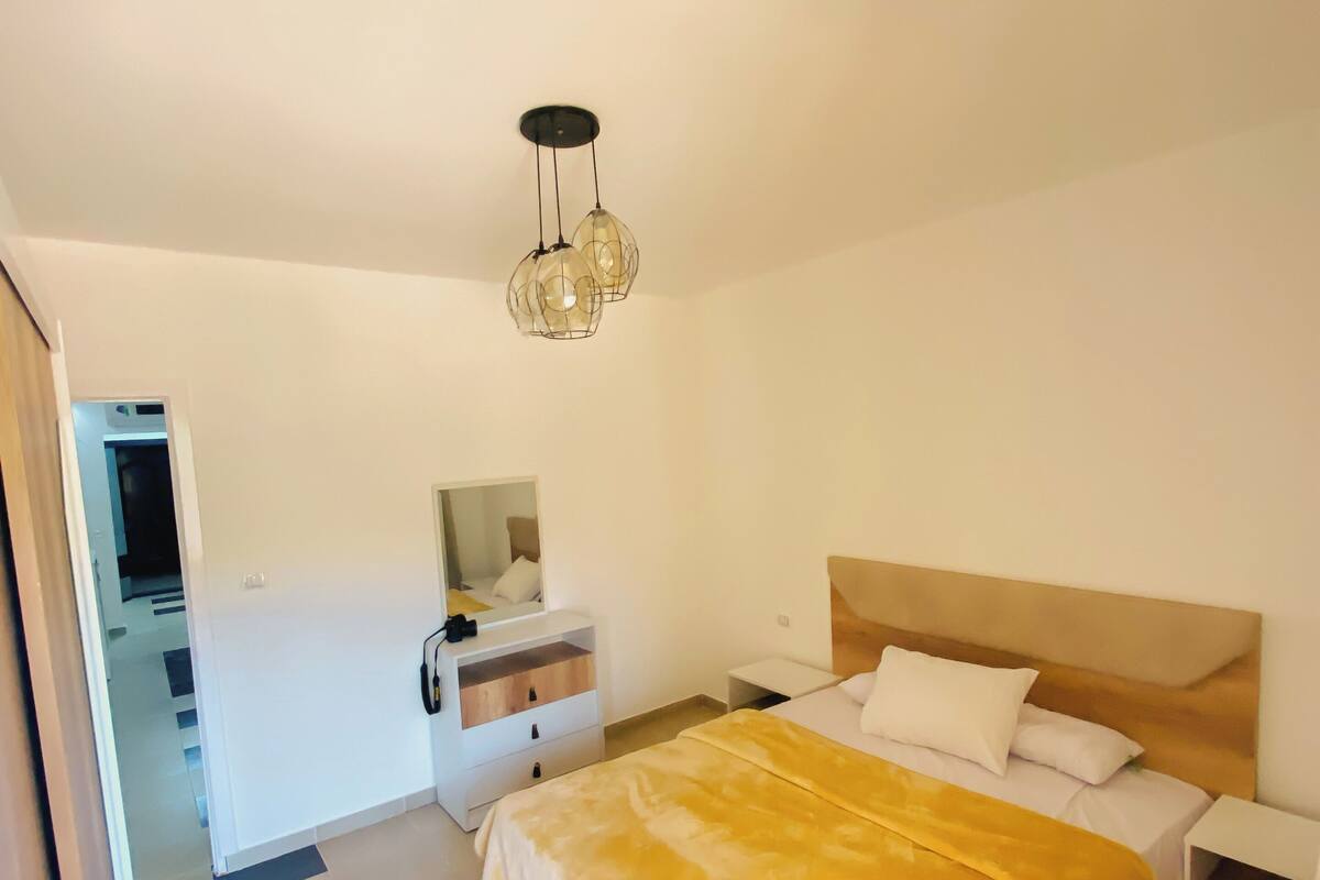 A bedroom with a bed, bedside tables, a dresser, a mirror, and a hanging light fixture.