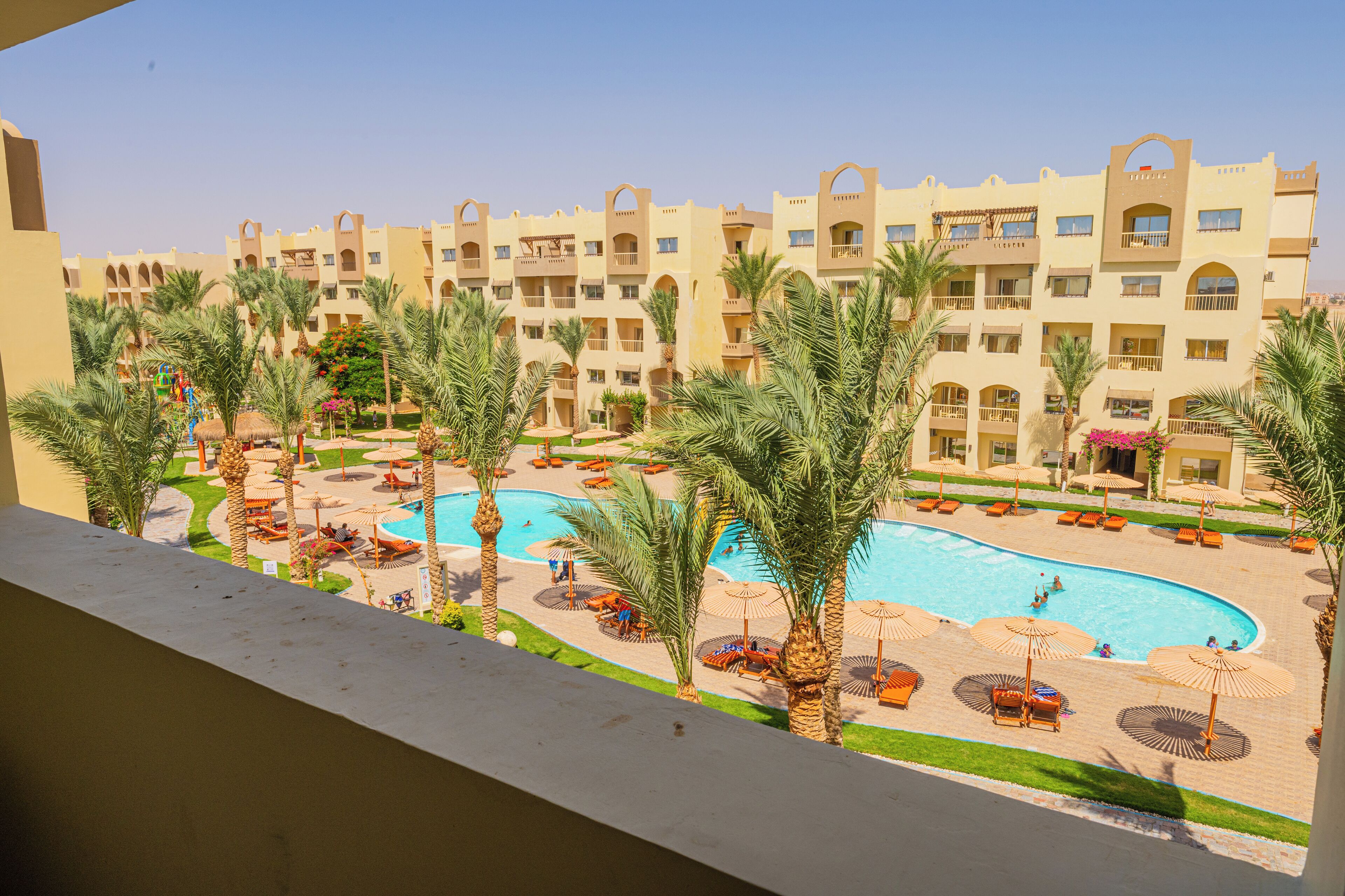 A hotel with a swimming pool surrounded by palm trees and sun loungers.