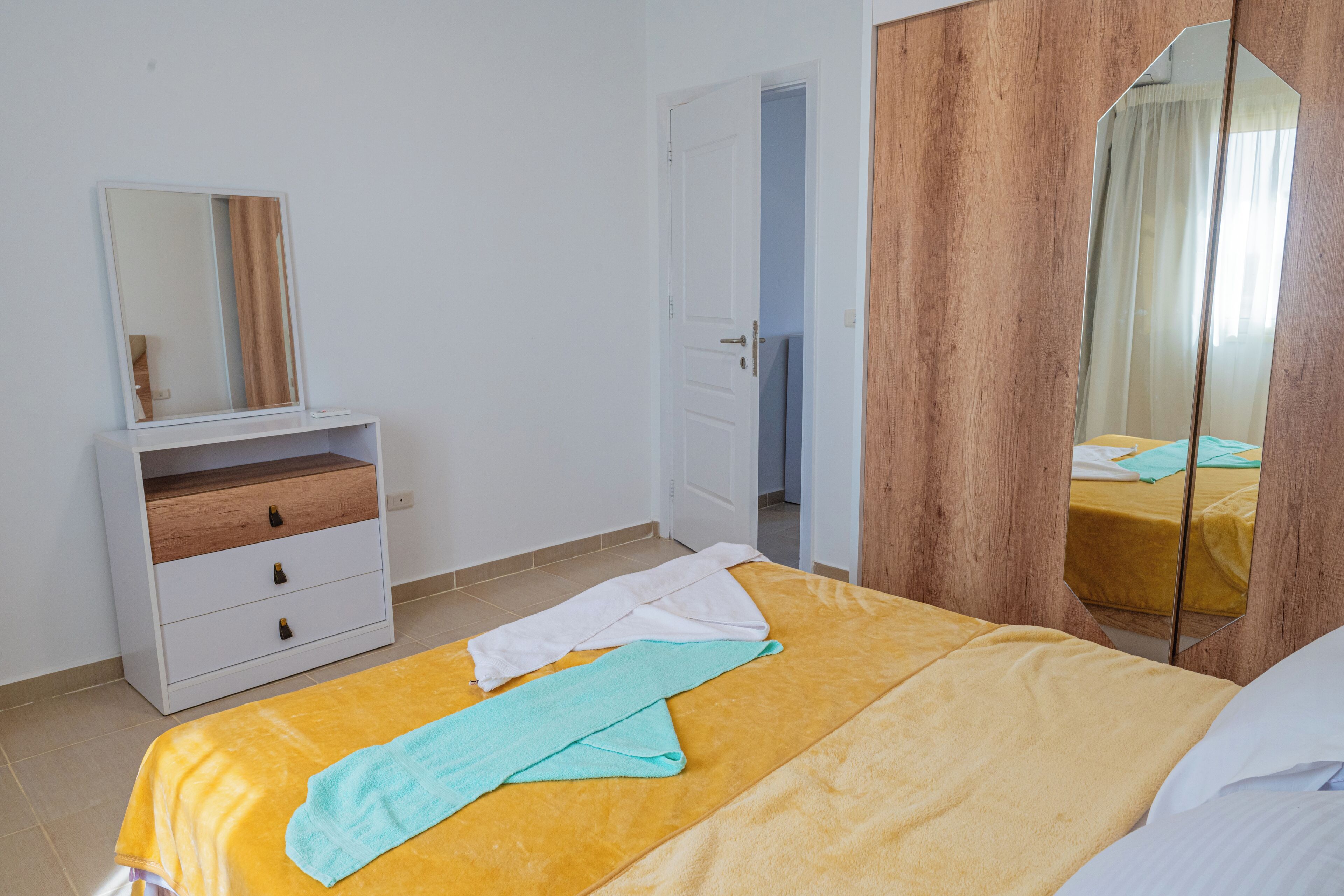 Une chambre à coucher comprenant un lit, une armoire en bois, un miroir et une porte donnant sur une autre pièce.
