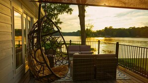 A deck with a hanging chair, a sofa, and a small table, overlooking a lake with a sunset view. - Luxurious large 3bd/2ba Home with Dock with beautiful sunset views (Eatonton)