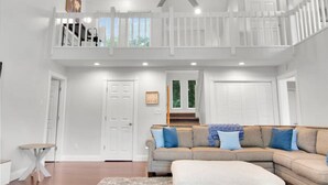 A spacious living room with a high ceiling, a ceiling fan, a large sectional sofa, a small table, and a staircase leading to an upper level. - Luxurious large 3bd/2ba Home with Dock with beautiful sunset views (Eatonton)