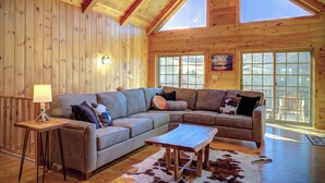 Una sala de estar acogedora con un sofá seccional, una mesa de centro de madera y grandes ventanales que ofrecen vistas al exterior.