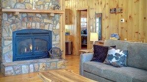 Interior acogedor de una cabaña con chimenea de piedra, paredes de madera y una zona de estar confortable.