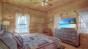 Un dormitorio de cabaña de madera con una cama, una silla, un tocador y un cuadro con una playa.
