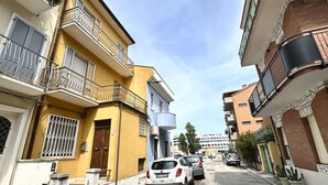 A narrow street with parked cars, a yellow building with a balcony, and a blue building with a curved facade. - P032 - Porto Recanati, sky-land 100 meters from the sea (Porto Recanati)
