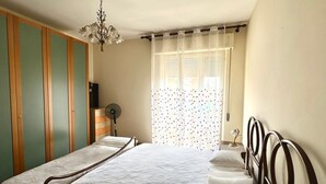 A bedroom with a bed, a dresser, a fan, a chandelier, and a window with curtains. - P032 - Porto Recanati, sky-land 100 meters from the sea (Porto Recanati)